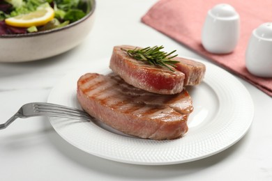 Photo of Delicious tuna steaks with rosemary on white marble table, closeup