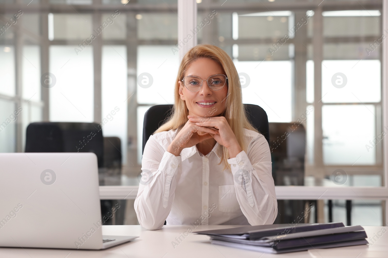 Photo of Smiling woman at table in office. Lawyer, businesswoman, accountant or manager