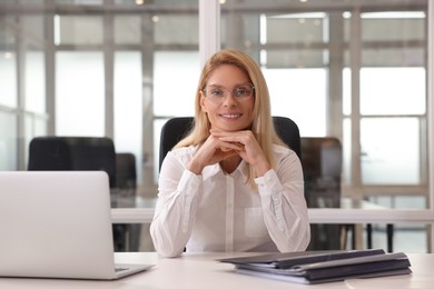 Photo of Smiling woman at table in office. Lawyer, businesswoman, accountant or manager