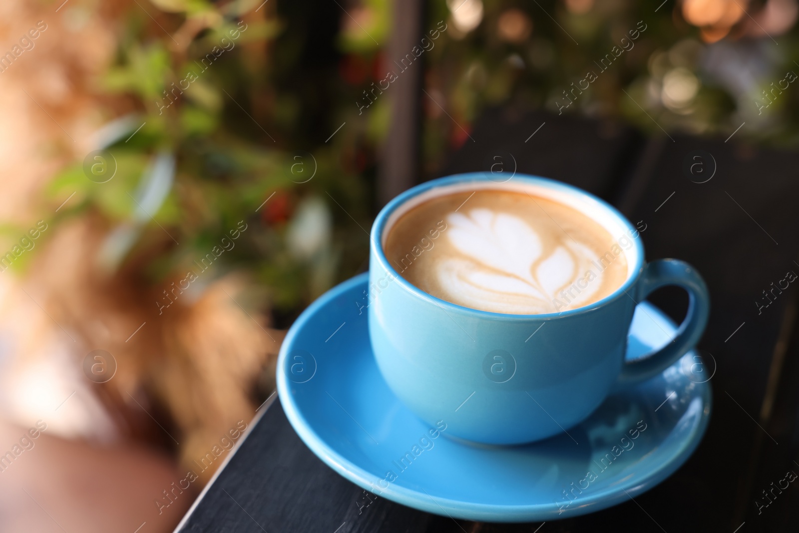 Photo of Ceramic cup of aromatic coffee with foam on wooden table in outdoor cafe. Space for text