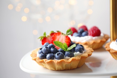 Photo of Tarts with different berries on cake stand. Delicious pastries