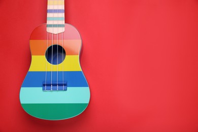Photo of Colorful ukulele on red background, top view and space for text. String musical instrument