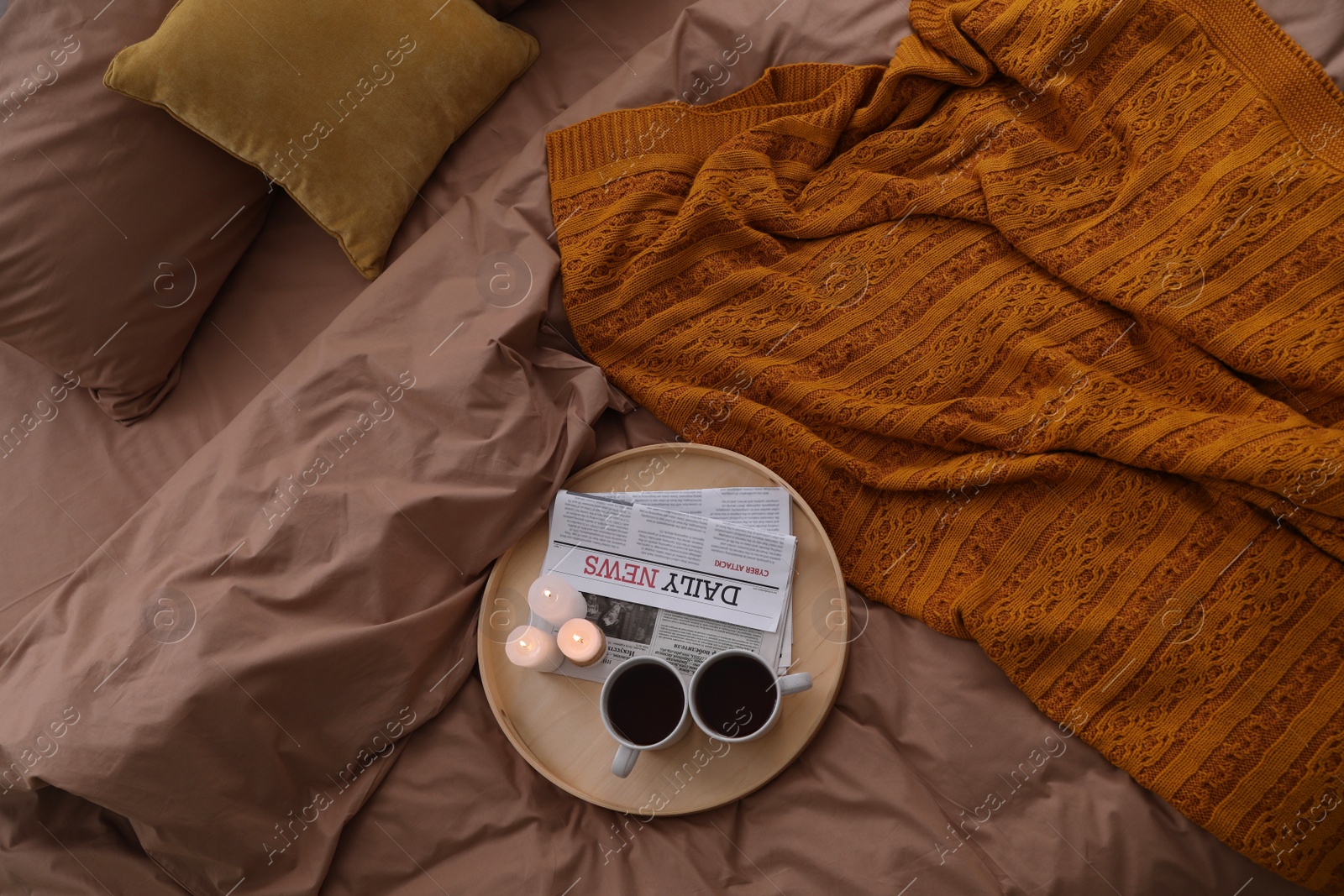 Photo of Cups of hot drink and candles on bed with brown linens, above view