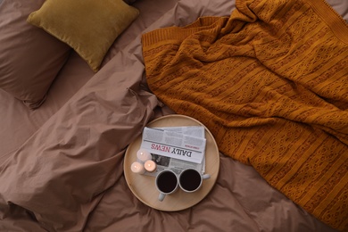 Cups of hot drink and candles on bed with brown linens, above view