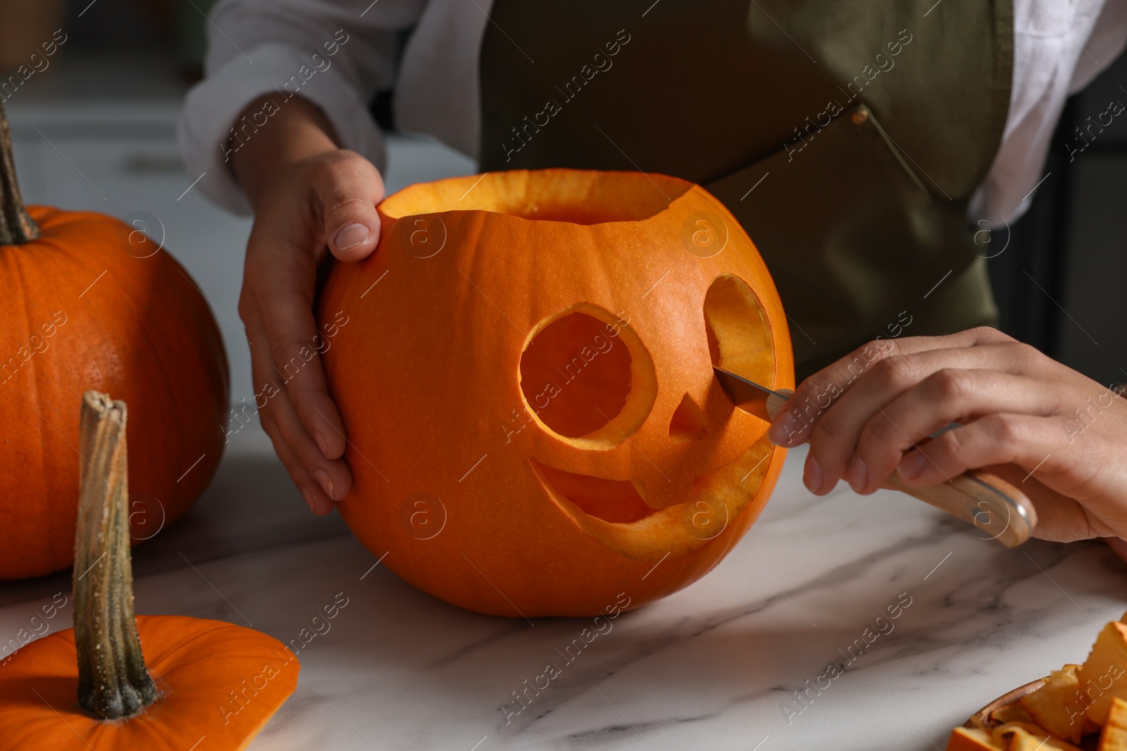 Photo of Woman carving pumpkin for Halloween at white marble table, closeup