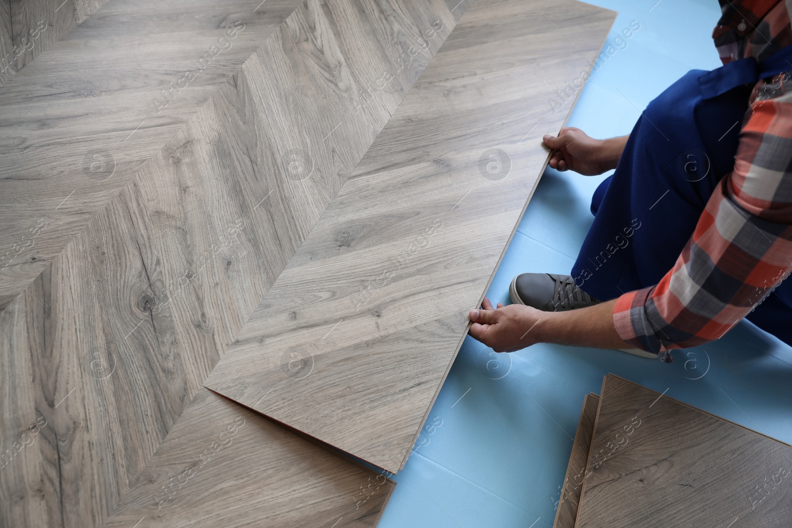 Photo of Worker installing laminated wooden floor indoors, closeup