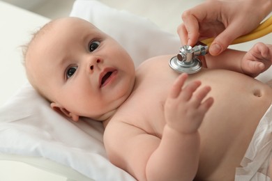 Photo of Pediatrician examining cute little baby with stethoscope in clinic, closeup