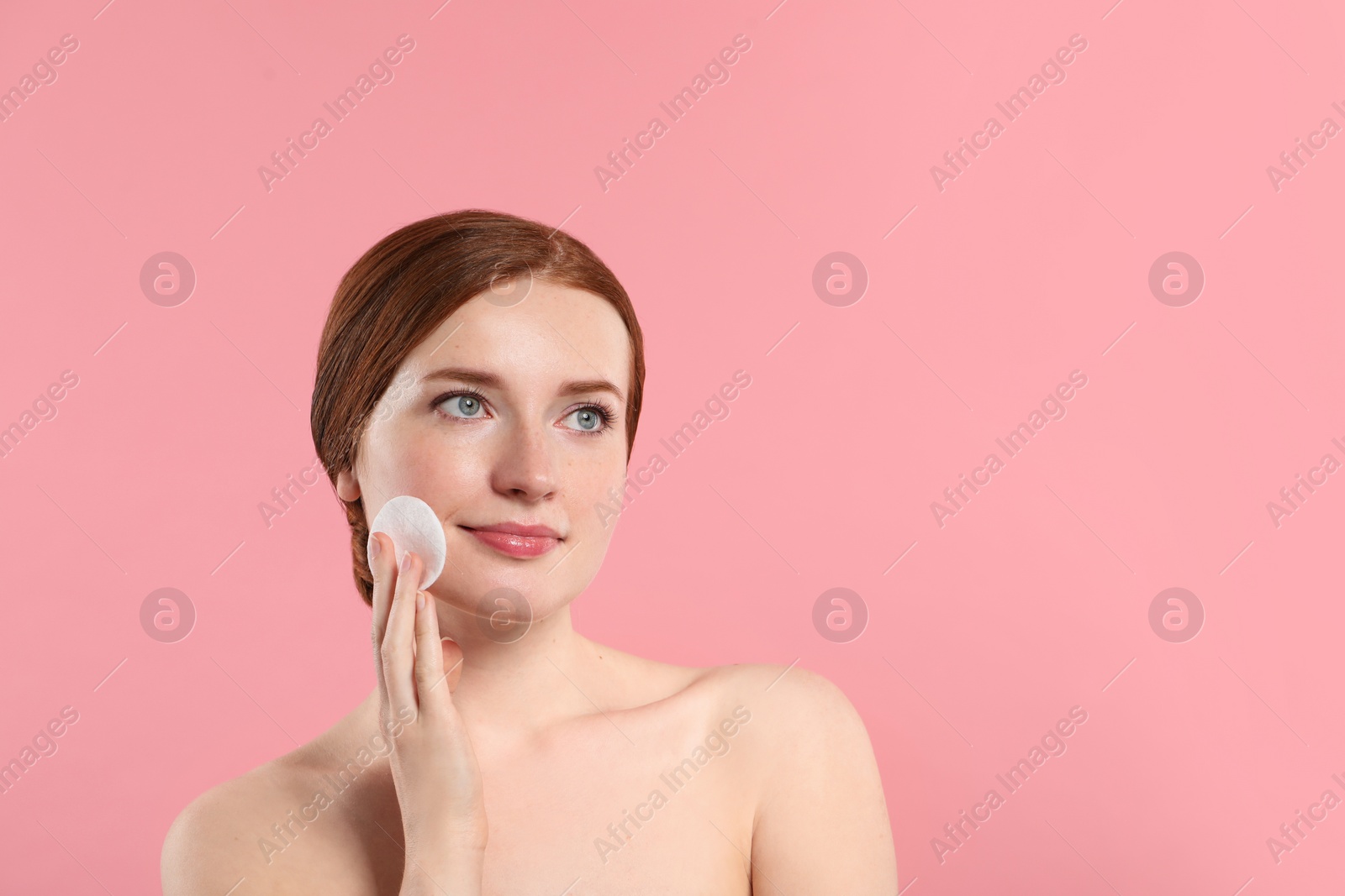 Photo of Beautiful woman with freckles wiping face on pink background. Space for text