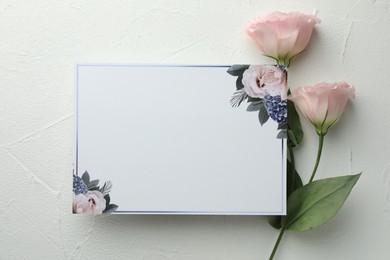 Blank invitation card and pink flowers on white table, flat lay