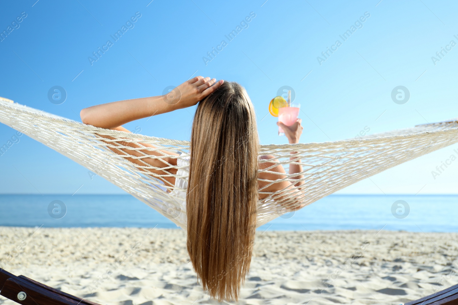 Photo of Young woman with refreshing cocktail relaxing in hammock on beach