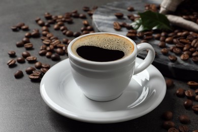 Cup of aromatic hot coffee and beans on grey table