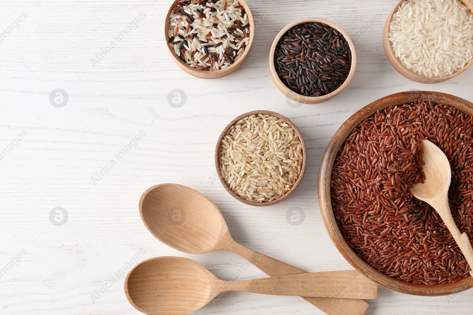 Photo of Flat lay composition with brown and other types of rice on white wooden background. Space for text