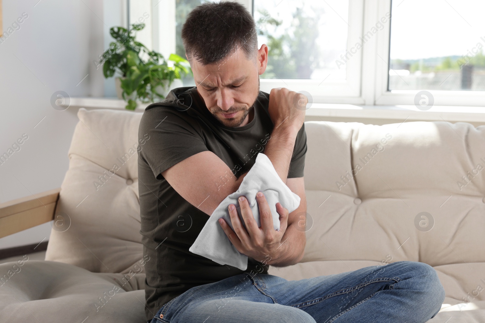 Photo of Man using heating pad on sofa at home