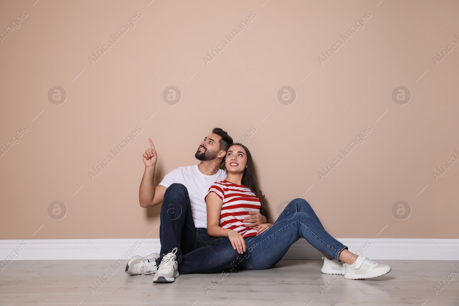 Photo of Young couple sitting on floor near beige wall indoors