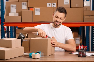 Photo of Post office worker with utility knife opening parcel at counter indoors