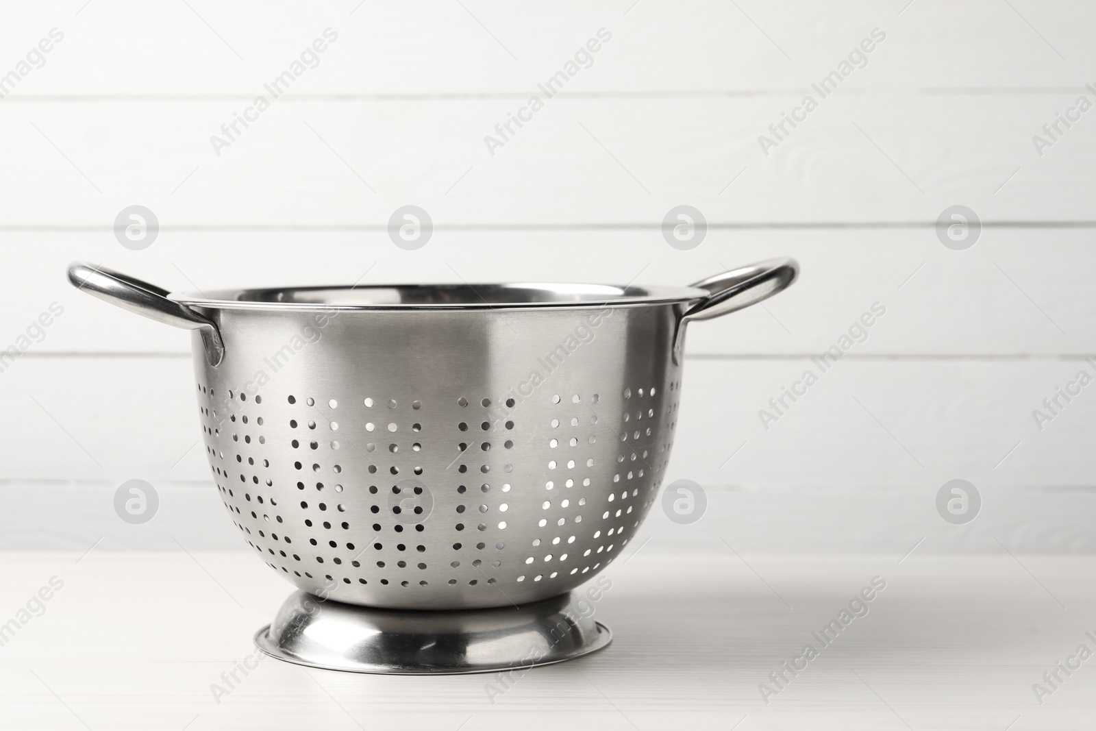 Photo of Metal colander on white wooden table. Space for text