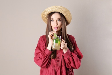 Emotional young woman drinking natural detox lemonade on beige background