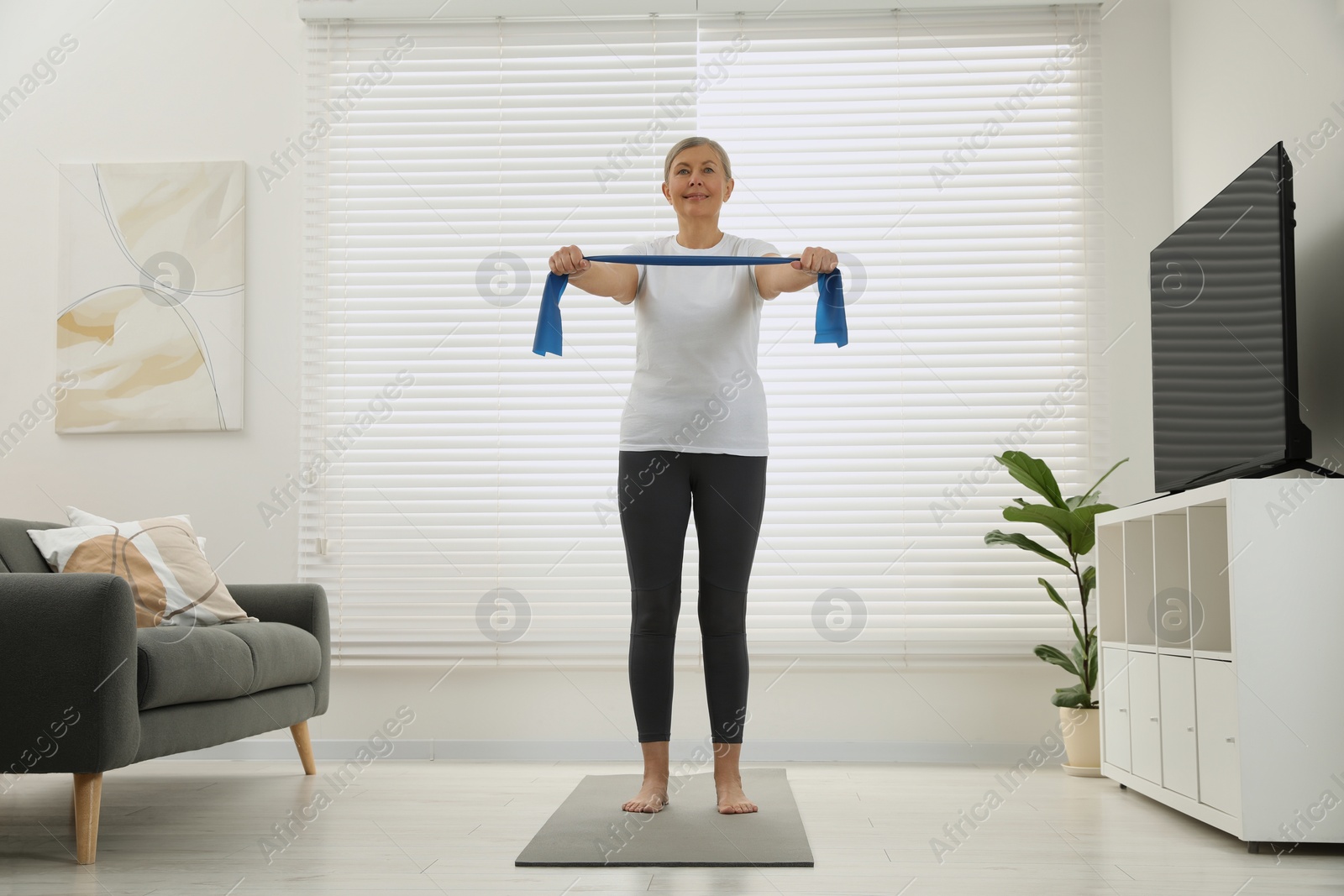 Photo of Senior woman doing exercise with fitness elastic band on mat at home