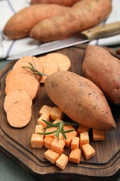 Photo of Wooden board with cut and whole sweet potatoes on table