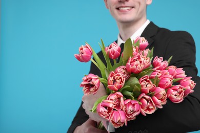 Photo of Happy man with beautiful bouquet on light blue background, closeup