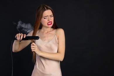 Stressed young woman with flattening iron on black background. Hair damage