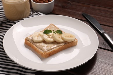 Toast with tasty nut butter and banana slices on wooden table, closeup