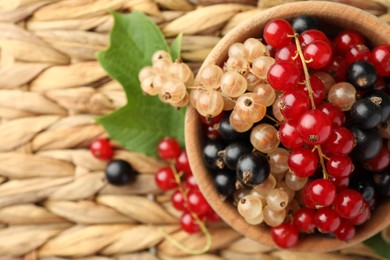 Photo of Different fresh ripe currants and green leaf on wicker surface, flat lay. Space for text