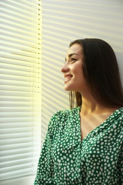 Photo of Young woman near window with Venetian blinds