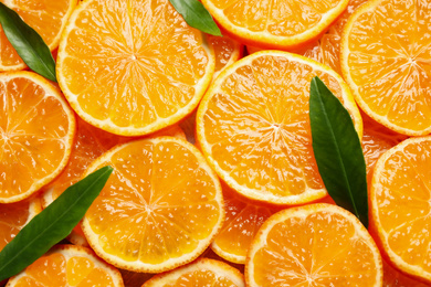 Slices of fresh ripe tangerines and leaves as background, top view. Citrus fruit