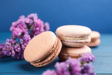 Photo of Delicious macarons and flowers on blue wooden table, closeup