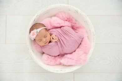 Photo of Adorable newborn girl lying in baby nest on light background, top view