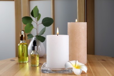 Photo of Burning candles, essential oil and plumeria flower on wooden table