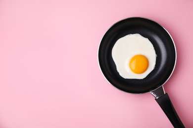 Tasty fried egg in pan on pink background, top view. Space for text