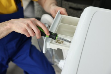 Photo of Plumber with screwdriver repairing washing machine indoors, closeup