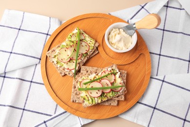 Fresh crunchy crispbreads with cream cheese, radish and green onion on beige table, top view