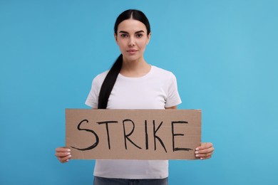 Woman holding cardboard banner with word Strike on light blue background