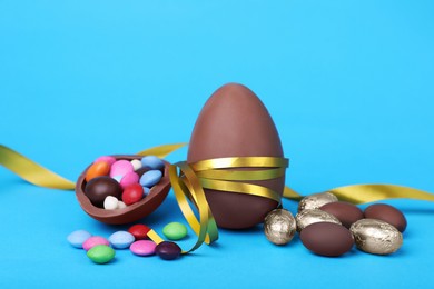 Photo of Delicious chocolate eggs and candies on light blue background