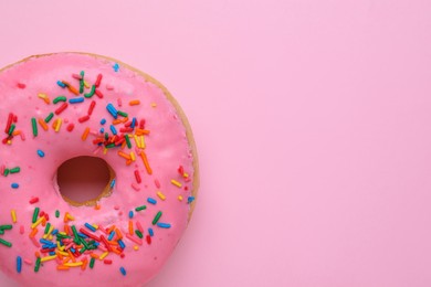 Photo of Tasty glazed donut decorated with sprinkles on pink background, top view. Space for text