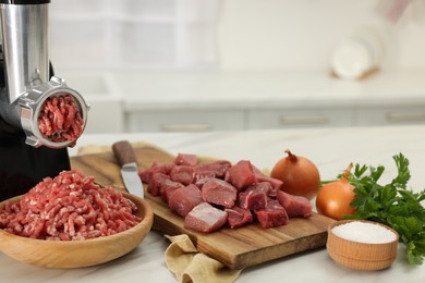 Photo of Electric meat grinder with beef and products on white marble table in kitchen