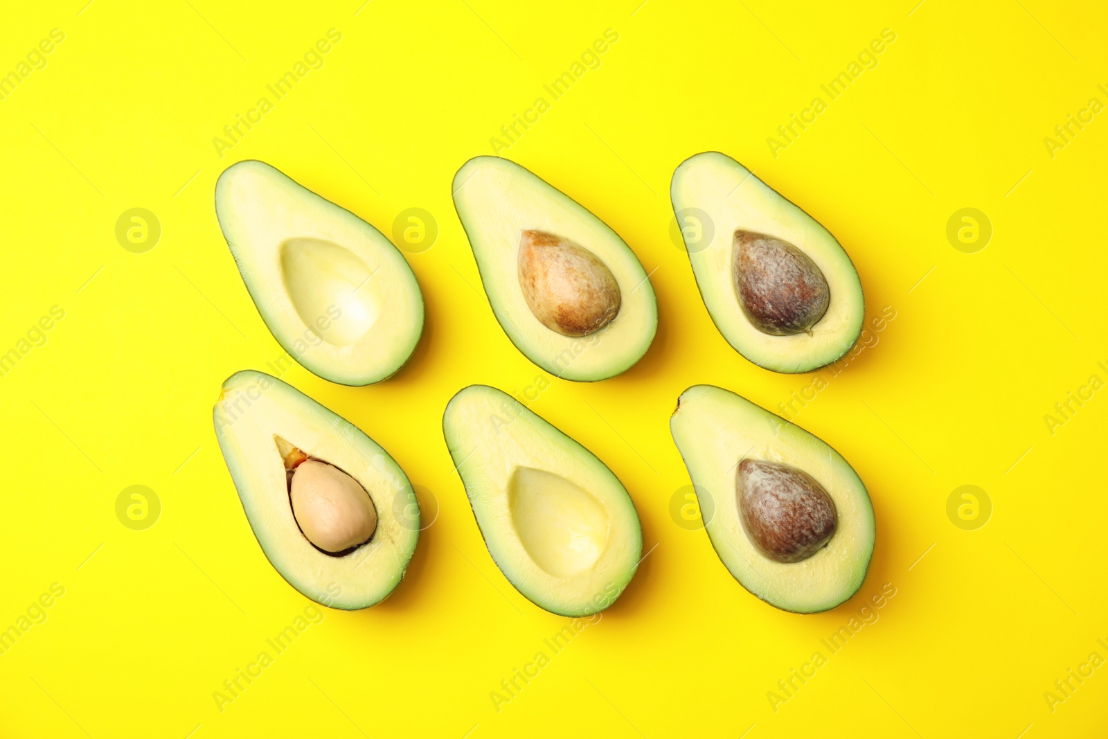 Photo of Cut fresh ripe avocados on yellow background, flat lay