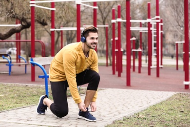 Photo of Young man with headphones tying shoelaces on sports ground