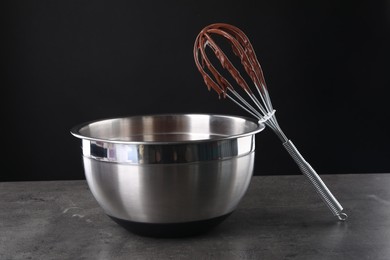 Photo of Bowl and whisk with chocolate cream on grey table against black background