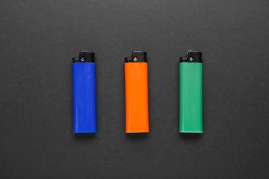 Stylish small pocket lighters on black background, flat lay