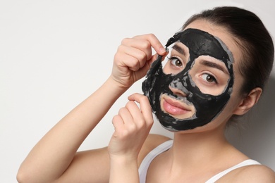 Photo of Beautiful young woman removing black mask from her face on white background