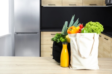 Photo of Tote bags with vegetables and bottle of juice on wooden table in kitchen. Space for text