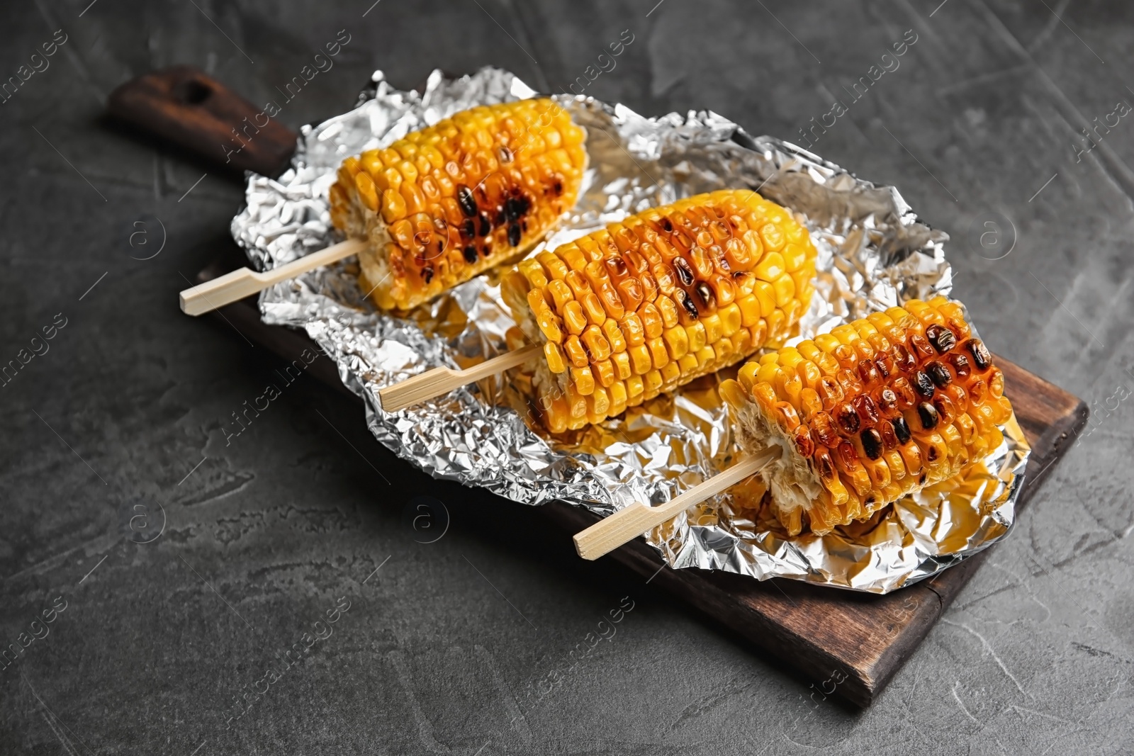 Photo of Foil with delicious grilled corn cobs on table