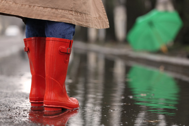 Woman in rubber boots walking outdoors on rainy day, closeup. Space for text