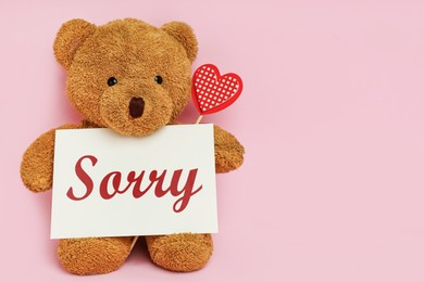 Image of Cute teddy bear holding card with word Sorry on pink background, space for text