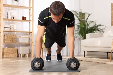 Photo of Handsome man doing plank exercise with dumbbells on floor at home