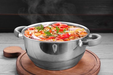 Saucepan of delicious vegetable soup with meat and ingredients on grey wooden table